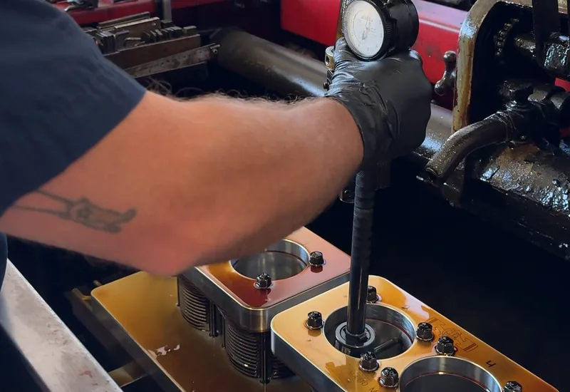 A machinist measuring a cylinder bore with a dial bore gauge through a bolted-on torque plate