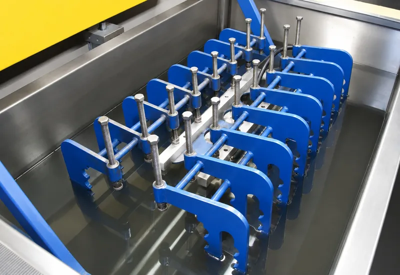 A rack of clamping fixtures lowered into a heated parts washing tank
